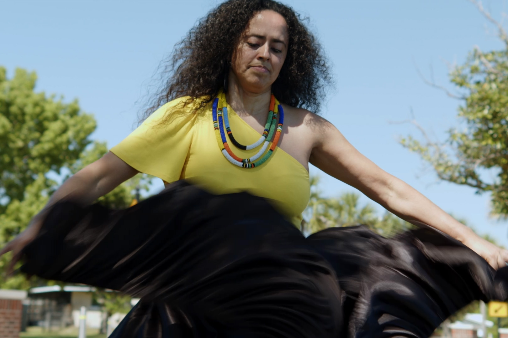 Woman dancing in colorful yellow top and dark flowing skirt