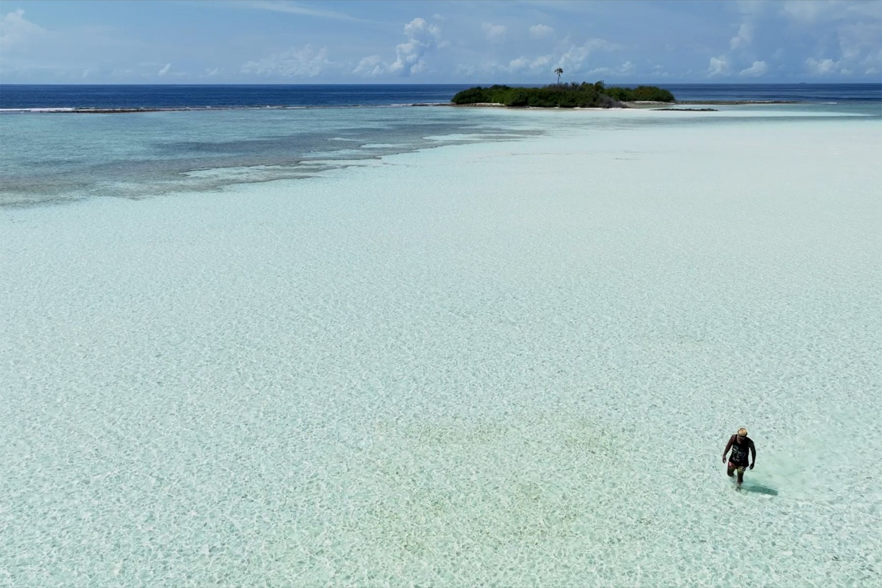 man walking through shallow clear ocean water