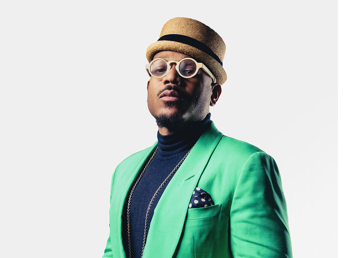 Man in green suit with round glasses and hat