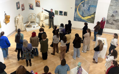 Man facing forward pointing at artwork on wall with back of people observing