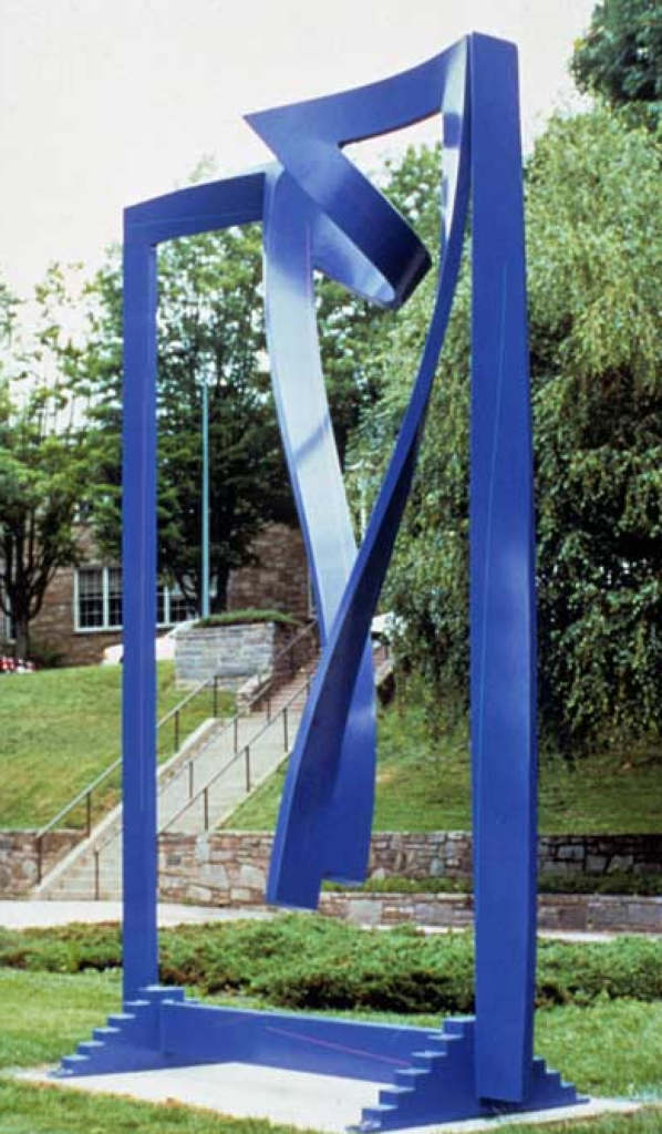A large, bright blue painted steel sculpture standing on a concrete pad on a grassy lawn. The sculpture forms a massive rectangular frame with miniature steps along the base, enclosing a central abstract ribbon of metal that dramatically twists and curls downward from the top. In the background, an outdoor staircase leads up a grassy slope toward campus trees and buildings.