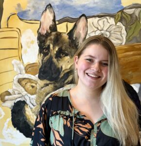 Picture of a blonde woman smiling in front of a painting